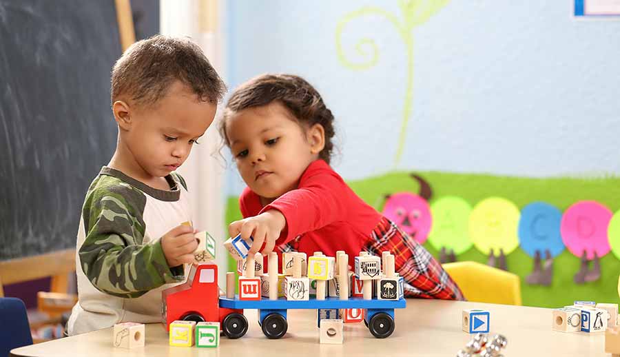 Two students play with blocks and trucks together.