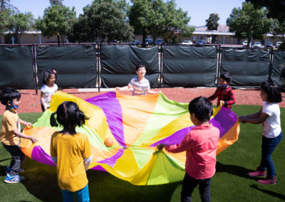 Children using a multi-colored tarp to bounce a ball around.