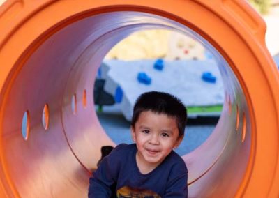 A young boy crawling through a large tube on the playground.