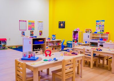 A large play area with group tables, toys, and a closet for dress-up clothes.