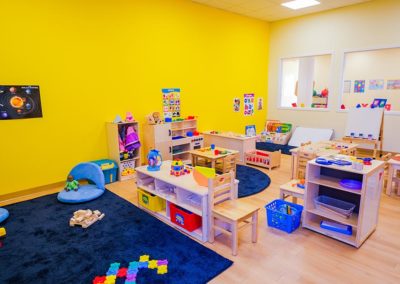 A large play area with group tables, toys, and a closet for dress-up clothes.