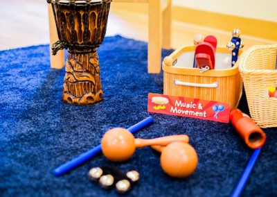 Floor space set up for Music & Movement lessons with a blue rug, instruments, and toys.
