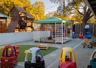 An outside play area with a covered gazebo, toy cars, and scooters.