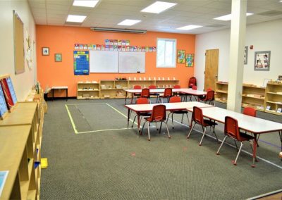 A Safari Kid classroom with wooden bookcases, whiteboards, and two large group tables.