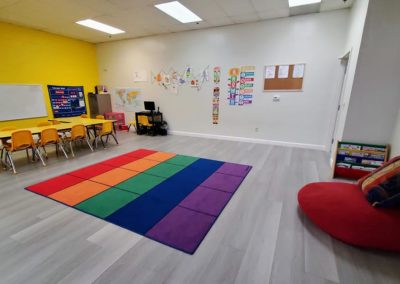 A Safari Kid classroom with a large colorful rug in the center of the room and a group table.
